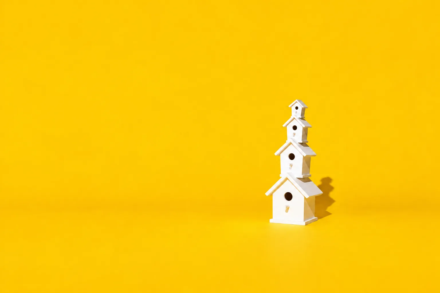 A tower of white birdhouses stacked on one another, each smaller than the last, on a yellow floor