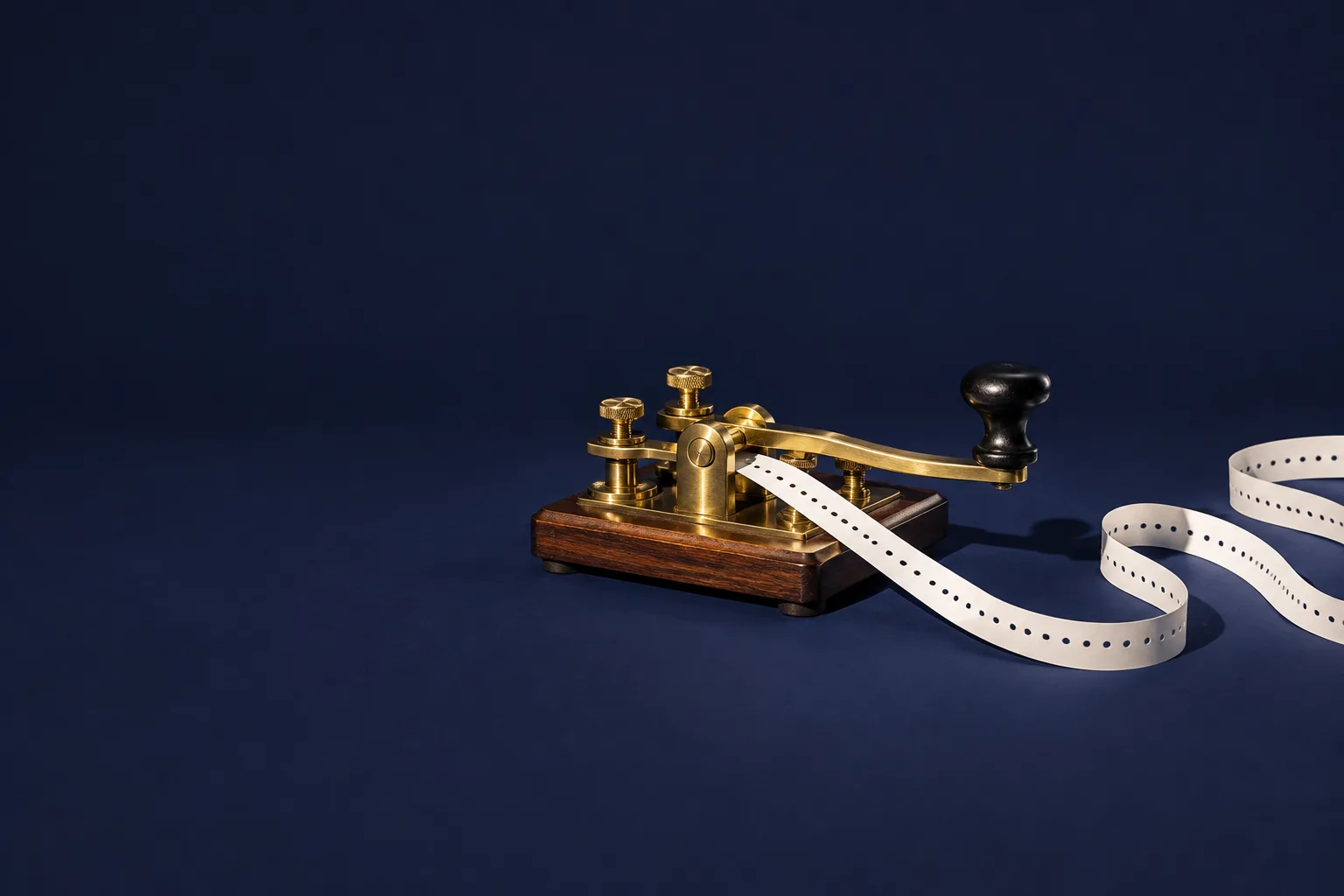 A brass telegraph key with a long punched paper tape looping out across a navy floor