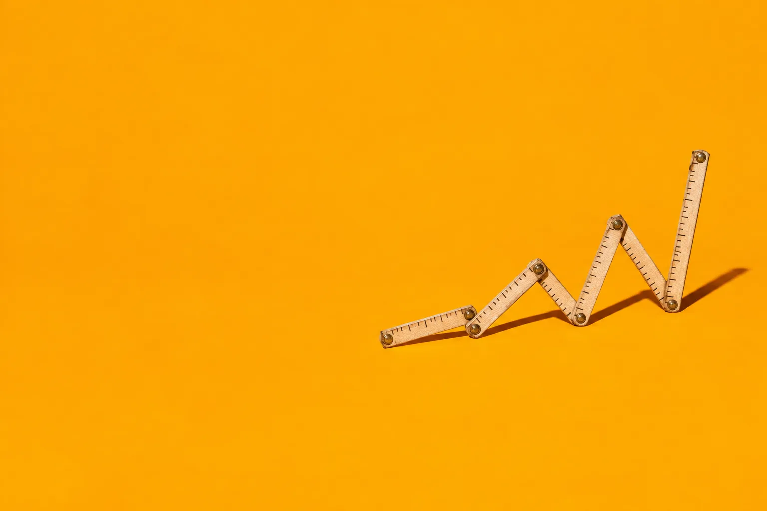 A wooden folding ruler zig-zagging upward like a growth chart on an orange floor