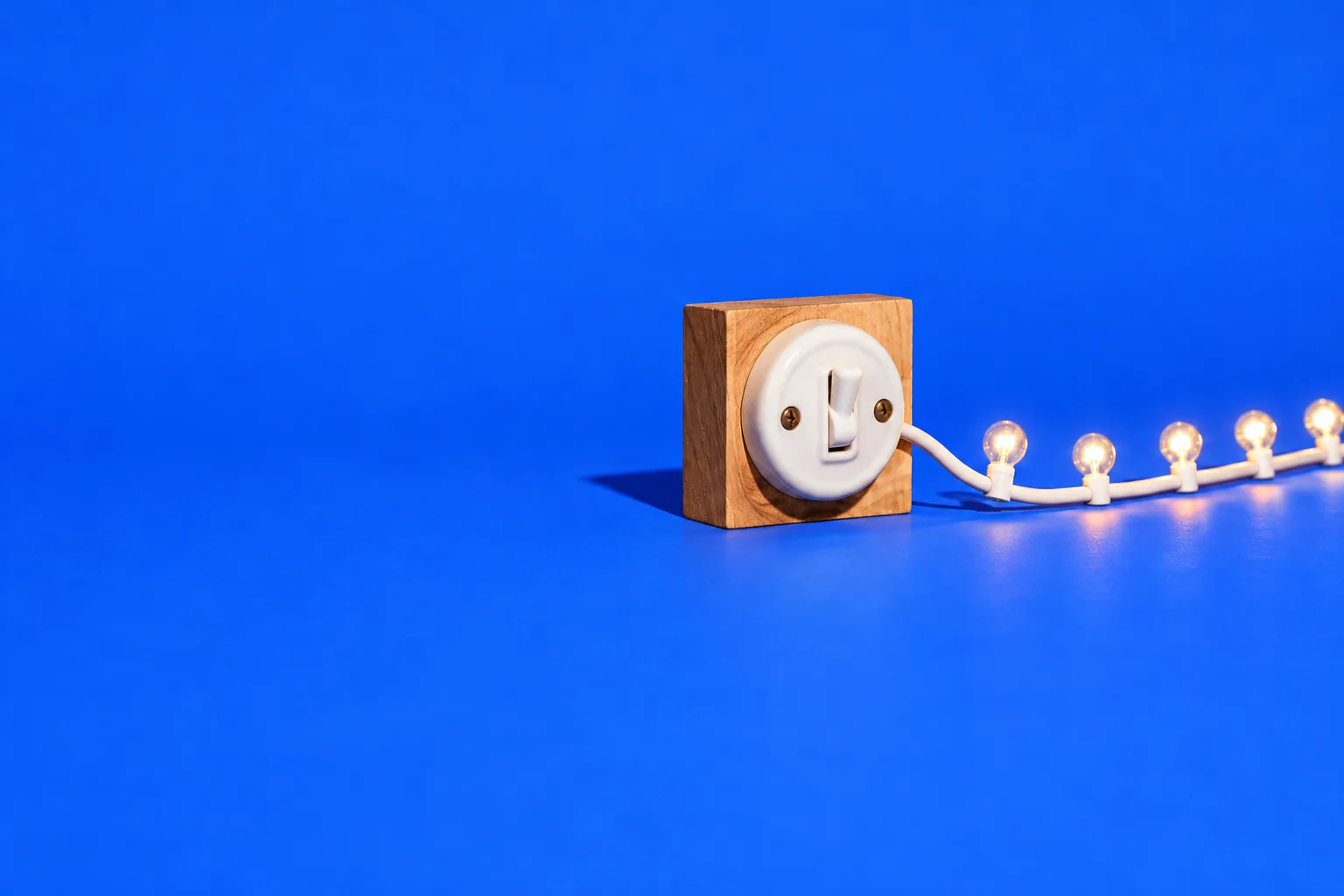 A vintage light switch flipped on, lighting a string of small bulbs across a blue floor