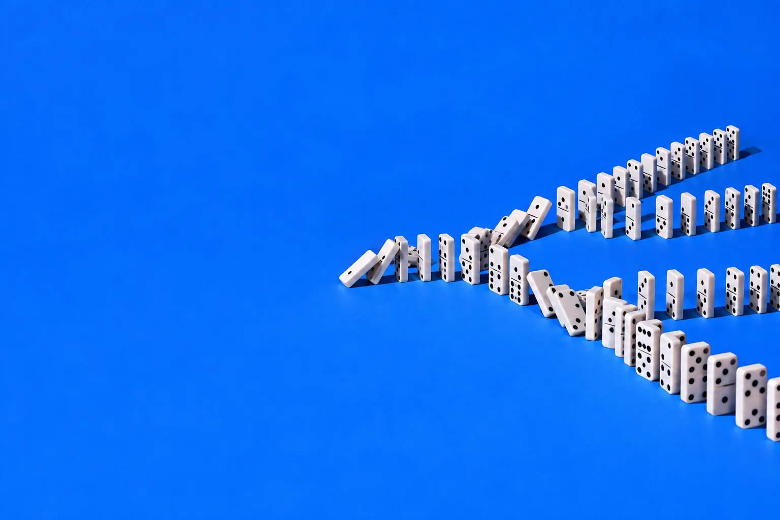 A line of white dominoes tipping over and splitting into more and more lines on a blue floor