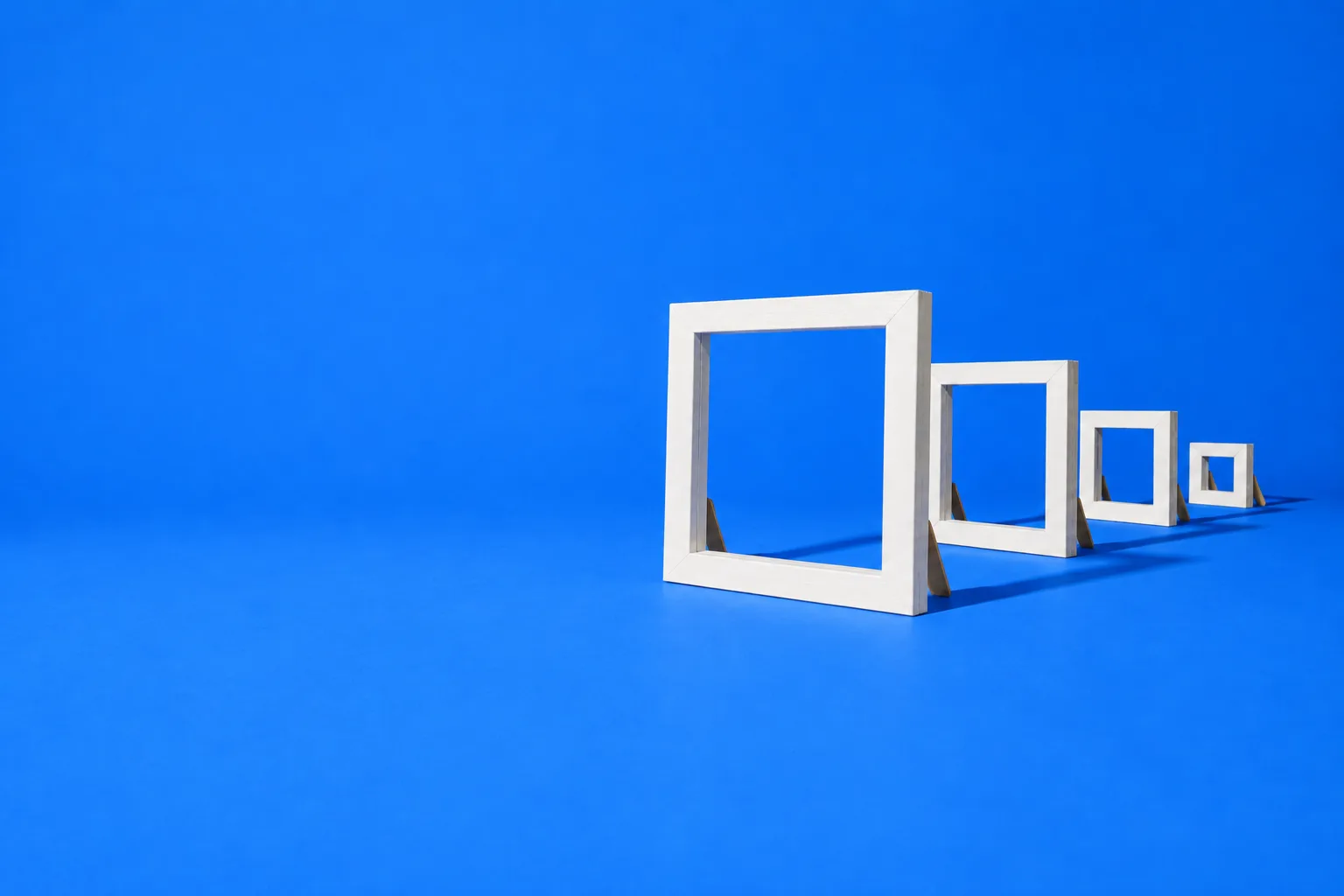 Four white picture frames standing in a row, each one framing the next smaller one, on a blue floor