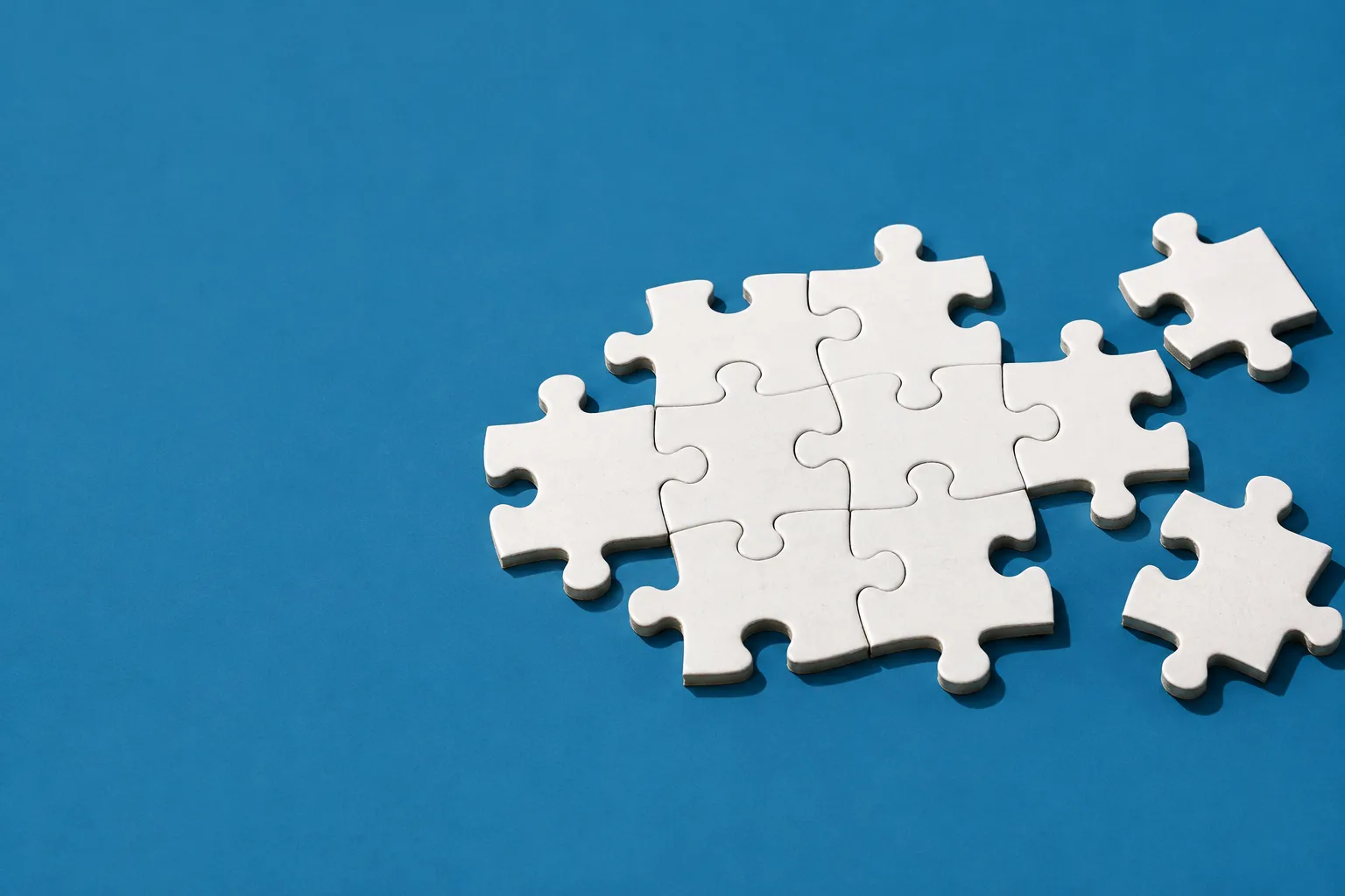 White jigsaw pieces locked together, with more pieces about to click into place, on a steel-blue floor